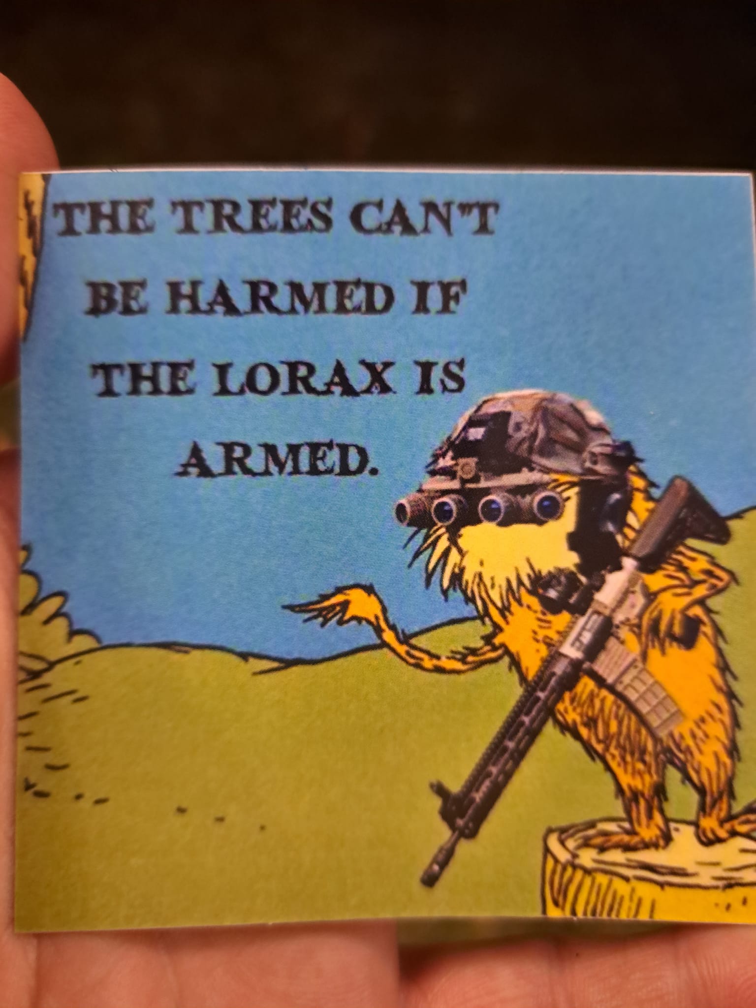 This meme is a humorous image featuring the character of the Lorax from Dr. Seuss, but with a twist. The image shows the Lorax, known for speaking up for the environment, holding a rifle and wearing a helmet, with a caption that reads: "The trees can't be harmed if the Lorax is armed." The meme is a play on the original Dr. Seuss story, where the Lorax is a voice for the environment, but in this version, he's taken on a more aggressive tone.